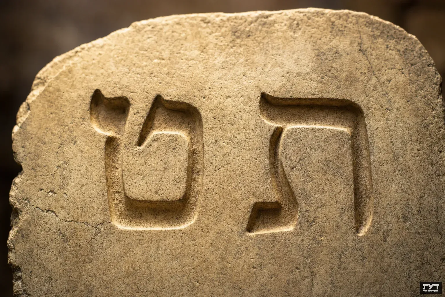 אותיות עבריות ט וב חקוקות באבן עתיקה עם תאורה חמה, הט משמאל והב מימין, רקע מטושטש