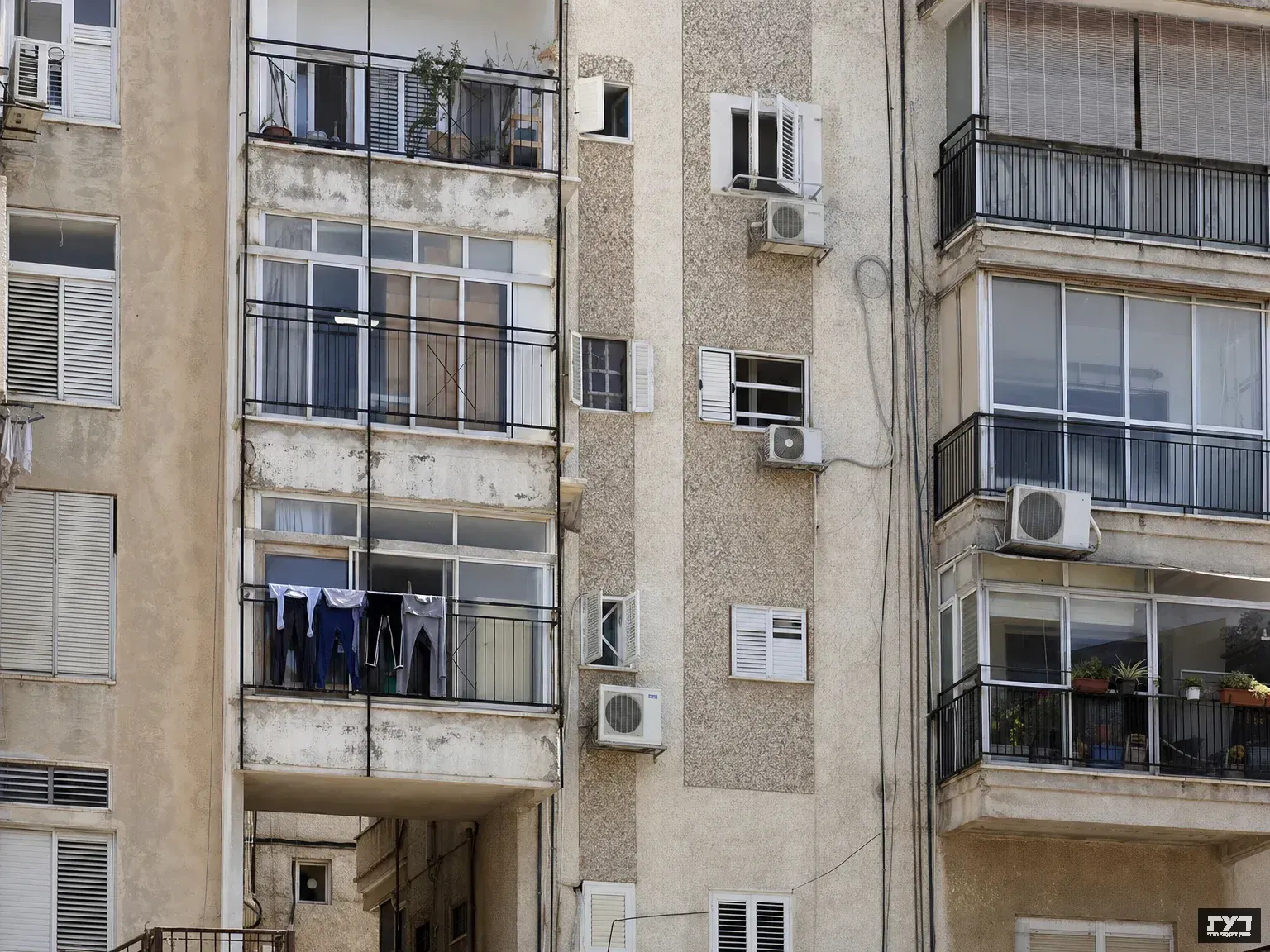 חזית בניין דירות ישראלי טיפוסי עם חלונות רבים, מרפסות, מזגנים וכביסה תלויה, משקף אתגרי דיור.