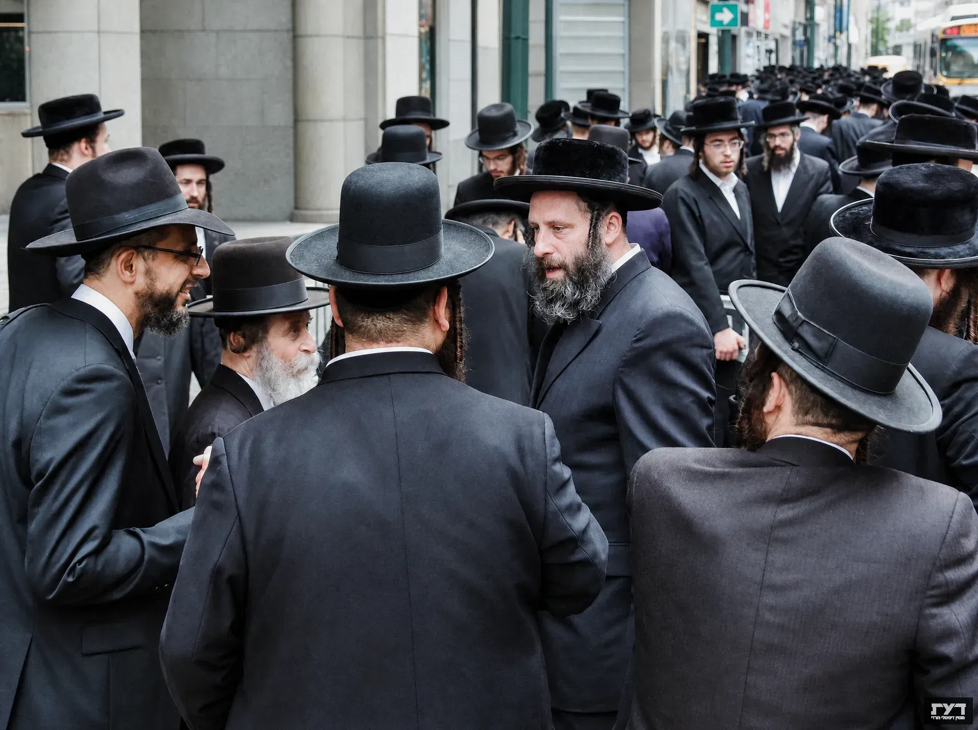 גברים חרדים בחליפות ומגבעות שחורות מתכנסים ברחוב עירוני